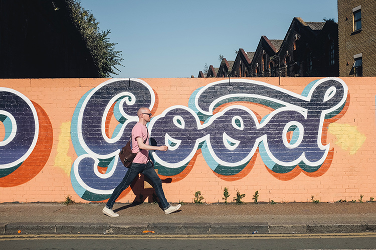 man walking in front of graffiti that says "good"